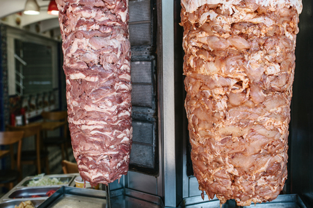 Raw foods for outdoor shawarma - two kinds of meat on vertical grill on kitchen background with vegetables in stainless steel containersの写真素材