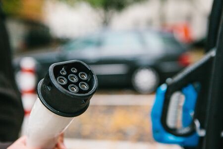The driver picks up a cable to charge the electric vehicle. A modern and eco-friendly mode of transport that has spread throughout the world.の写真素材