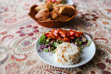 Vegetable salad with rice and cake with sesame seeds on patterned tableclothの写真素材