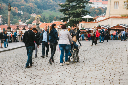 Prague, October 28, 2017: Unidentified woman is carrying disabled person in wheelchair along the Prague street, full of tourists next to the Prague Castleのeditorial素材