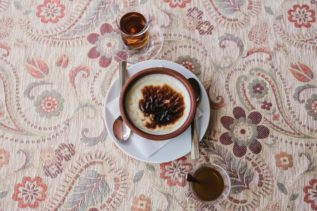 A baked rice dessert in a plate on the table next to a cup of fragrant hot tea in a cafe.の写真素材