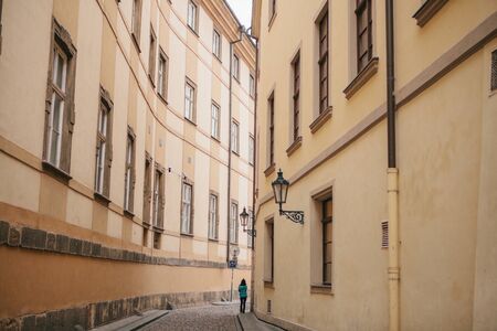 Tourist girl in green jacket walks along beautiful deserted narrow street in Prague between two historic buildingsの写真素材