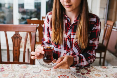 Beautiful young girl sitting at table in an outdoor cafe and drinking tea from glass beakerの写真素材