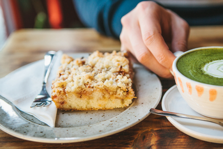 Close-up mans hand holding mug of green tea with beautiful pattern in the form of white foam next to dessertの写真素材