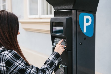 A modern terminal for paying for car parking. A young woman presses a button and tries to pay for a car parking. Modern technology in everyday life.の写真素材