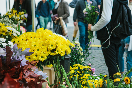 Street flower shop. In the foreground there are beautiful yellow and other flowers. The guy is holding a bouquet of flowers and is going to give them to his girlfriend at a meeting in the backgroundの写真素材