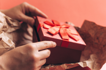 The girl has received a gift in a beautiful red box with a ribbon and is going to open it.