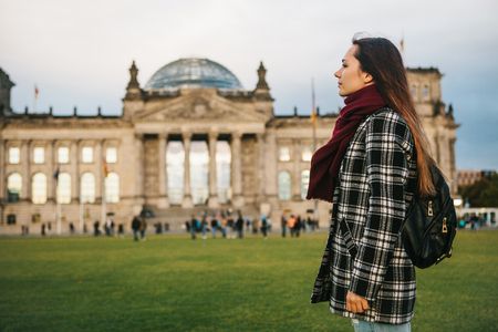 A tourist girl with a backpack next to the building called the Reichstag in Berlin in Germany. Sightseeing, tourism, travel around Europeの写真素材