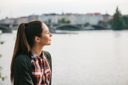 Young beautiful girl on the bank of the Vltava river in Prague in the Czech Republic, admiring the beautiful view and dreaming.の写真素材