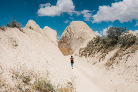 A tourist girl walks along the road next to the wonderful hills of Cappadocia in Turkey and admires the beauty around. The landscape of Cappadocia.の写真素材
