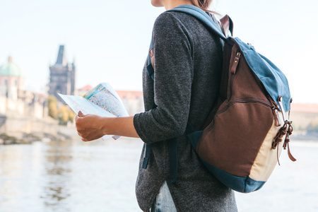 A young beautiful girl stands and looks at the map next to the Vltava River with the amazing old architecture of Prague in the background with a sunny spring dayの写真素材