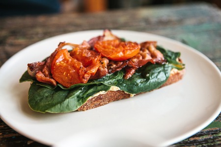 Delicious and nutritious sandwich with ham, fried tomato and greens on a plate on a wooden table.の写真素材