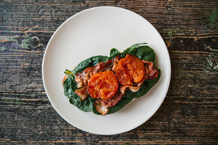 Top view. Delicious and nutritious sandwich with ham, fried tomato and greens on a plate on a wooden surface.の写真素材