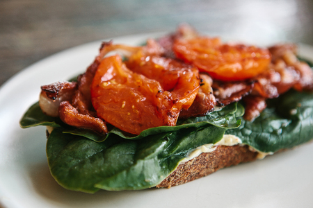 Close up delicious and nutritious sandwich with ham, fried tomato and greens on a plateの写真素材