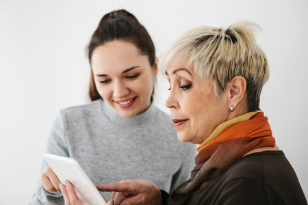 A young girl explains to an elderly woman how to use a tablet or shows some application or teaches you how to use a social network. Teaching the older generation of new technologies.の写真素材