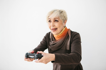 An elderly woman plays a video game and gestures that she won. Elderly person and modern technology.
