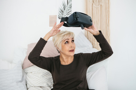 An elderly woman is going to put on virtual reality glasses to use them to immerse in the virtual world. The older generation and new technologies.の写真素材