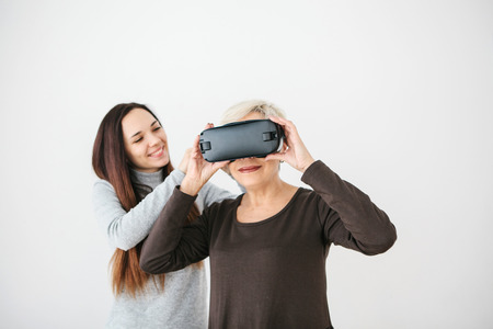 A young girl explains to an elderly woman how to use virtual reality glasses. The older generation...