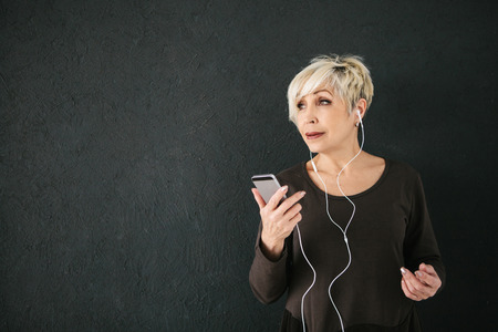 Positive elderly woman listening to music. On a dark background. The older generation and new technologies.の写真素材
