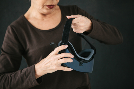 An elderly woman is going to put on virtual reality glasses to use them to immerse in the virtual world. The older generation and new technologies.の写真素材