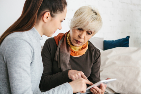 A young girl explains to an elderly woman how to use a tablet or shows some application or teaches you how to use a social network. Teaching the older generation of new technologies.の写真素材