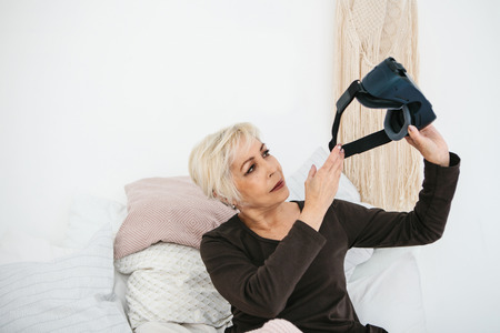 An elderly woman is going to put on virtual reality glasses to use them to immerse in the virtual...