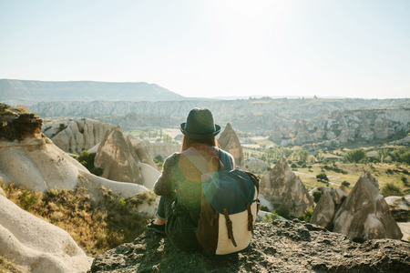 A tourist girl in a hat sits on a mountain and looks at the sunrise.の写真素材
