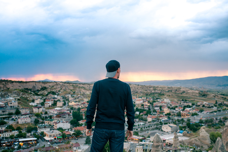 Young man tourist from a high point looking at the sunset over the city of Goreme in Cappadocia in Turkey and dreaming. Tourism, vacations, rest.の写真素材