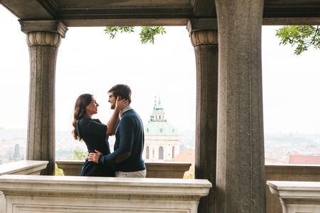A loving young beautiful couple of students from Europe embrace and communicate at the observation deck in Prague next to the columns. Close feelings and emotions between people.の写真素材