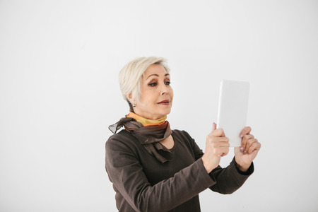 A positive modern elderly woman holds a tablet in her hands and uses it. The older generation and...