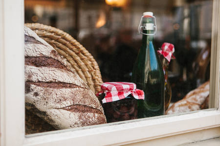 Homemade bread, a bottle of wine or other drink, a jar of jam at the glass in a cafe or a farmhouse. Window decorationの写真素材