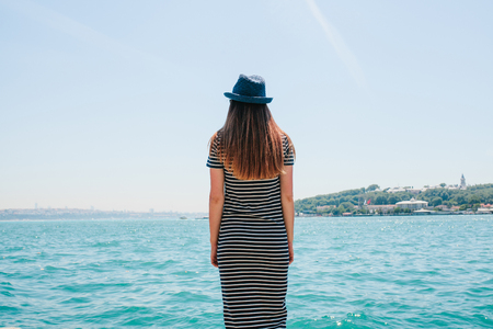 A young beautiful girl in a hat is enjoying a holiday in Turkey and beautiful views of the Bosphorus and Istanbul in the distanceの写真素材