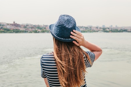 A young beautiful girl in a hat is enjoying a holiday in Turkey and beautiful views of the Bosphorus and Istanbul in the distanceの写真素材