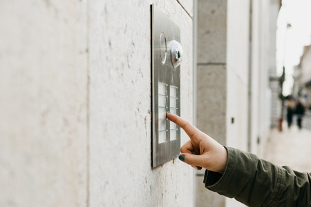 Close up the female hand presses the doorphone button. The girl is calling the intercomの写真素材