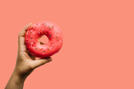 A female hand holds a donut on a red background. Creative idea.の写真素材