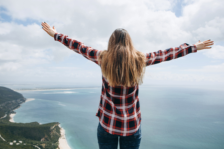 A girl or a tourist stands on top and admires a beautiful view of the sea or ocean coast and raises...