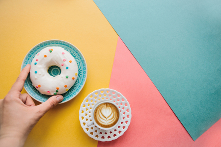 The girl is going to drink coffee and eat donut which lie on the colored surface.の写真素材