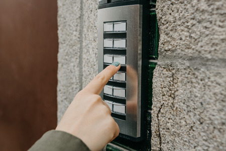 Close up the female hand presses the doorphone button. The girl is calling the intercom. Means of communication or notification of arrival and security of the entrance inside.の写真素材