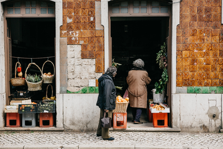 Elderly people or mature women shop at a street store in Lisbon, Portugal. Purchase of fresh food or economical purchases. Everyday life or routine in Europe.の写真素材