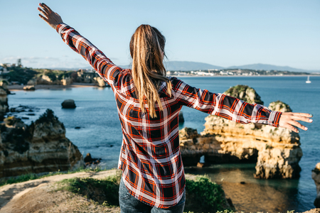 The girl admires a beautiful view of the Atlantic Ocean off the coast of Portugal next to the city called Lagos and raises her hands showing how she likes it and how she is free.の写真素材