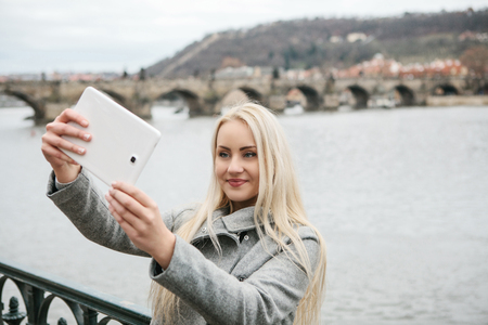 A beautiful young blond woman or tourist doing selfie or photographing herself in Prague in the Czech Republic. Charles Bridge in the background.の写真素材