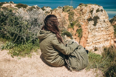 View from the back. A young woman tourist enjoys the beautiful views of the Atlantic Ocean and the landscape off the coast in Portugal.の写真素材