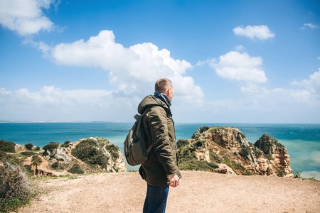 A tourist or traveler with a backpack walks along the coast of the Atlantic Ocean and admires the beautiful view of the ocean near the city called Lagos in Portugal.の写真素材