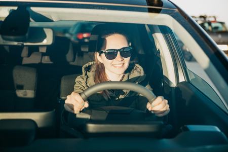 Portrait of a young smiling joyful woman or girl driver inside the car. Daily trips on transport or tourism, road travel or adventure.の写真素材