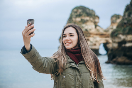A positive tourist girl takes a beautiful view or does a selfie or communicates with someone online using a cell phone.の写真素材