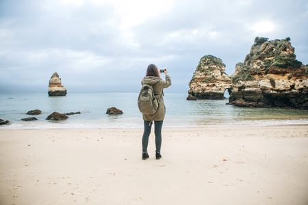 Girl tourist with a backpack photographing a beautiful landscape standing on the Atlantic coast.の写真素材