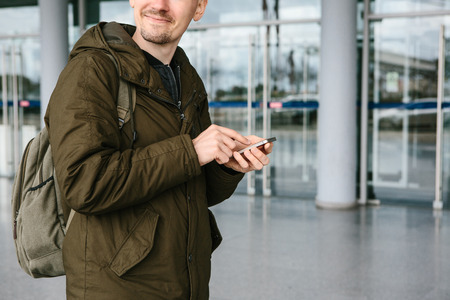A young male tourist at the airport or near a shopping center or station calls a taxi or talks on a cell phone or communicates with friends using a mobile phone.の写真素材