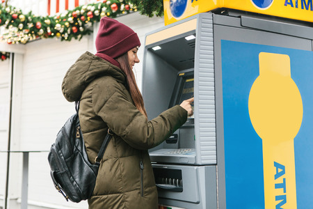 A young woman tourist or girl takes money from an ATM in Prague in the Czech Republic during the Christmas holidays for further tourism around the city.の写真素材