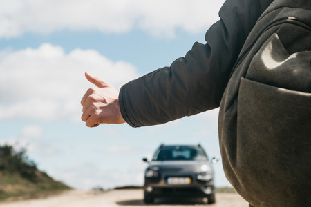 Close-up of a man hiker with a backpack hitch-hiking. He raised his finger up and tried to stop the car to continue his journey.の写真素材