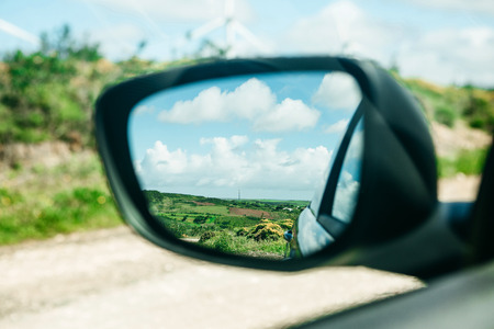 Close-up of a car rear view mirror in which a beautiful blue sky and a rural landscape. Traveling in the countryside.の写真素材